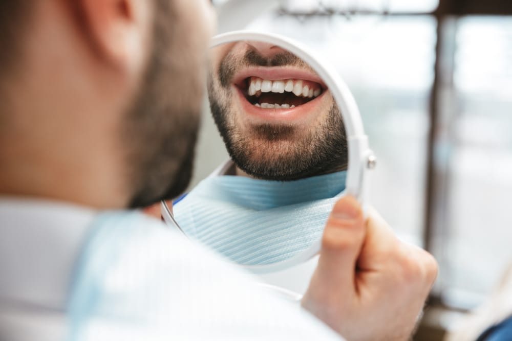 A man looking in the mirror at his teeth after undergoing laser dentistry treatments